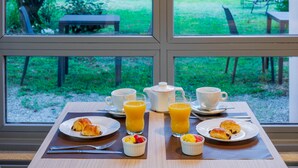 Una mesa de desayuno con cruasanes, fruta y jugo de naranja, con vista a un jardín exuberante a través de una ventana.