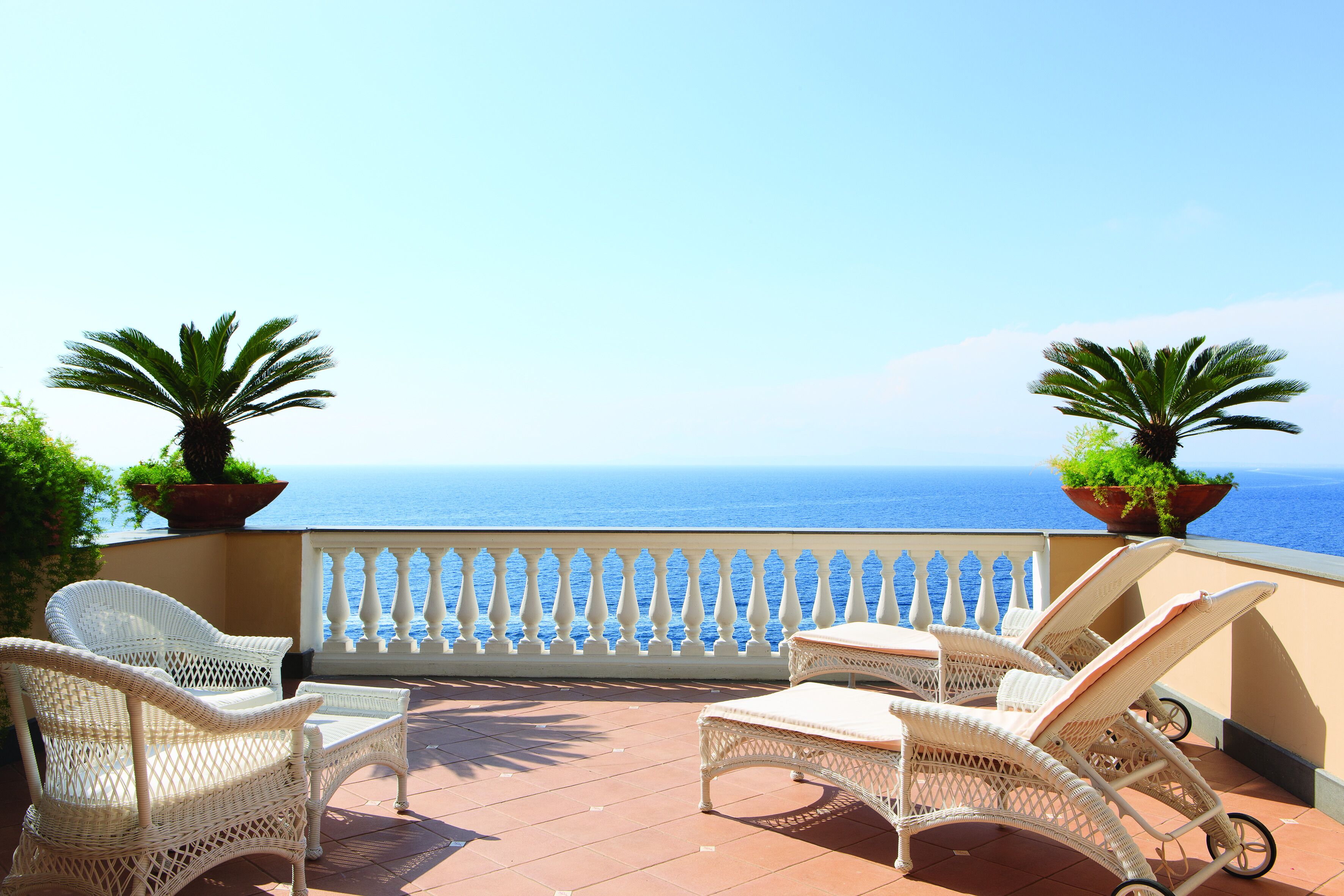 A terrace with wicker furniture and potted plants, overlooking a body of water.
