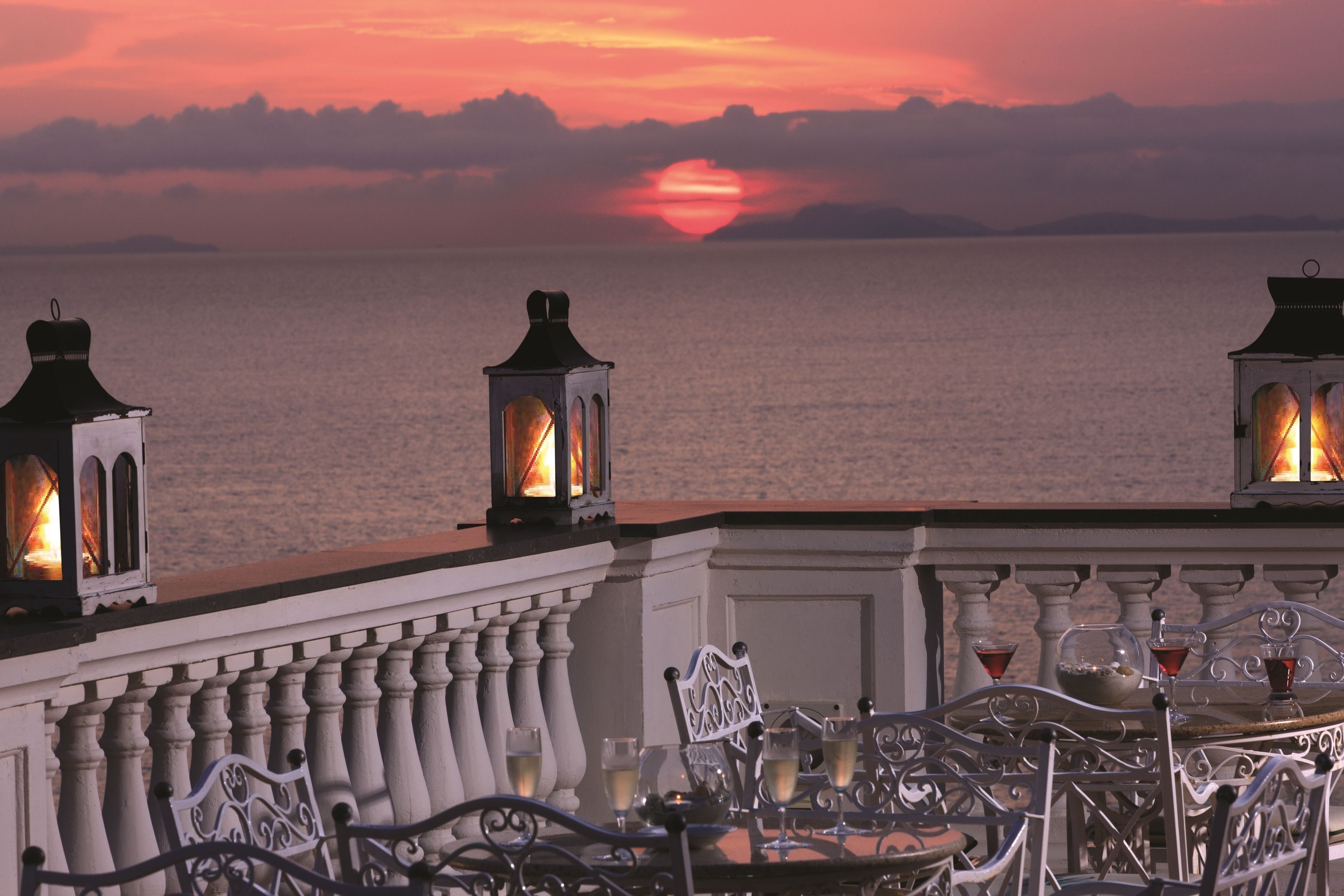 A terrace with a sunset view, outdoor seating, and lanterns.