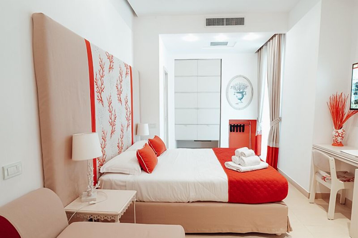 A modern hotel room with a large bed, a bedside table, a chair, and a desk with a chair.