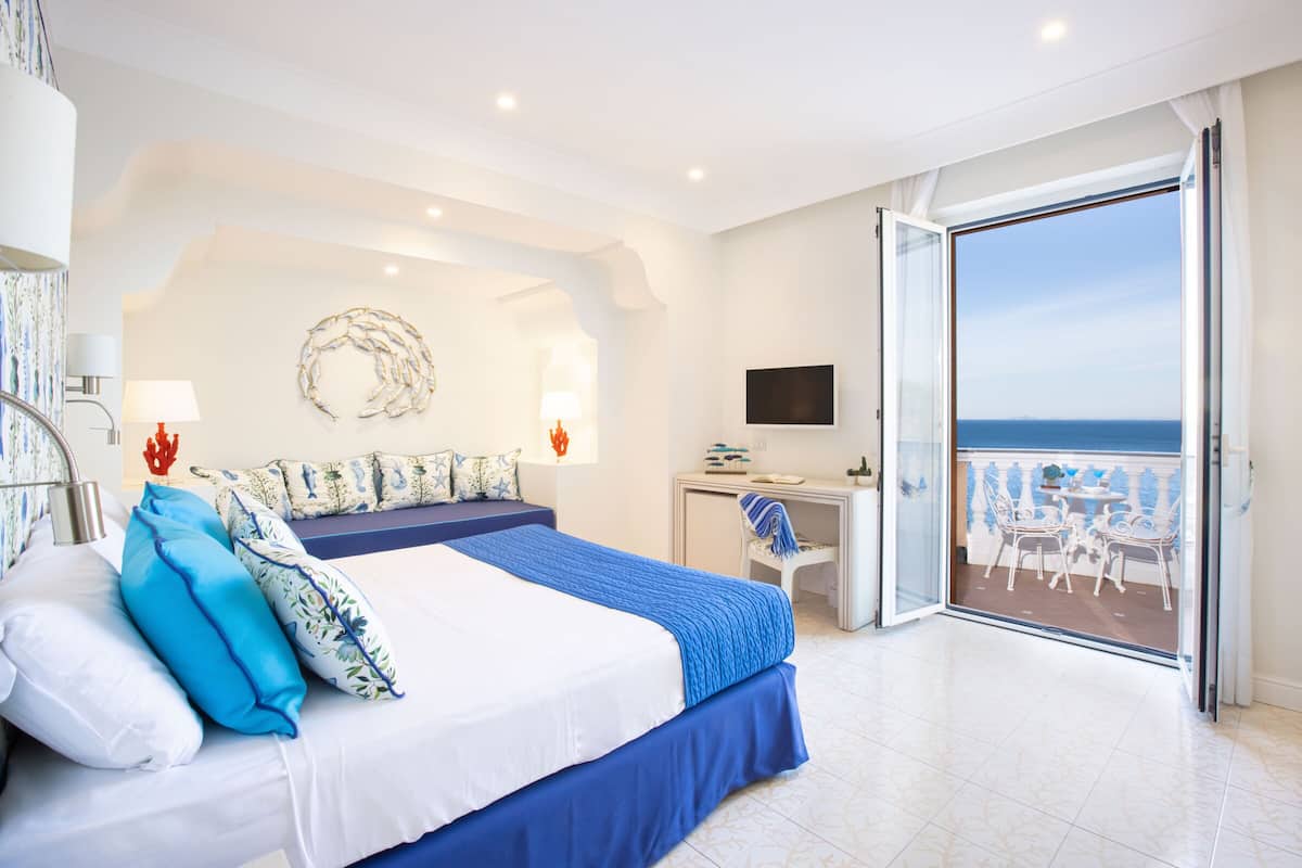 A bedroom with a bed, a desk, and a balcony with chairs.