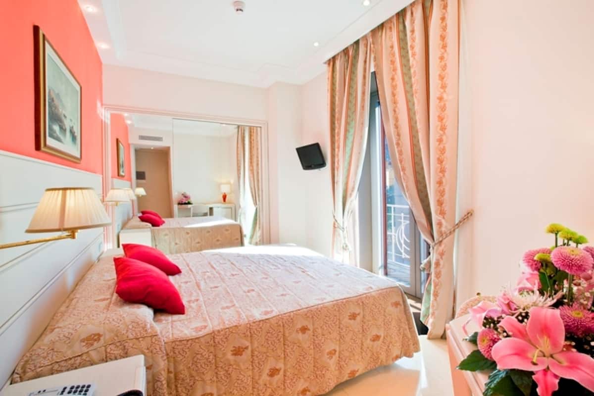 A hotel room with a large bed, a bedside table, a mirror, and a window with curtains.