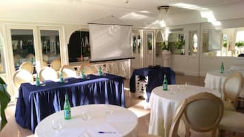 A formal dining room with round tables, chairs, and a projection screen.