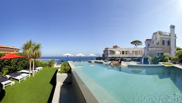 A pool area with clear blue water, lounge chairs, and umbrellas, overlooking a coastal view.