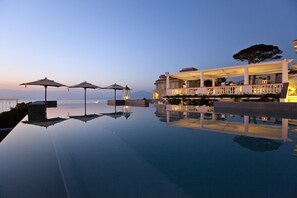 A serene infinity pool reflecting a clear sky, with umbrellas and a well-lit building in the background. - Hotel Corallo Sorrento (Sant'Agnello)