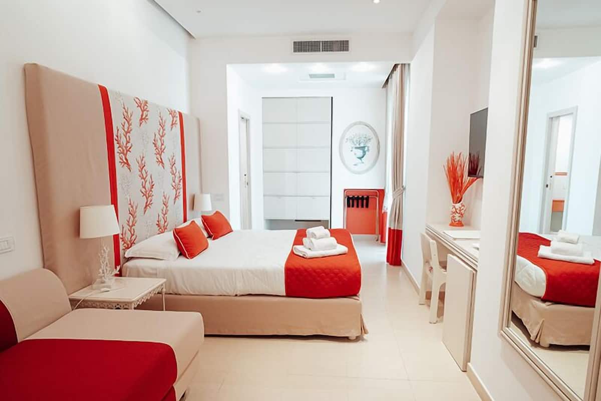 A hotel room with a large bed, a desk, a chair, and a mirror.