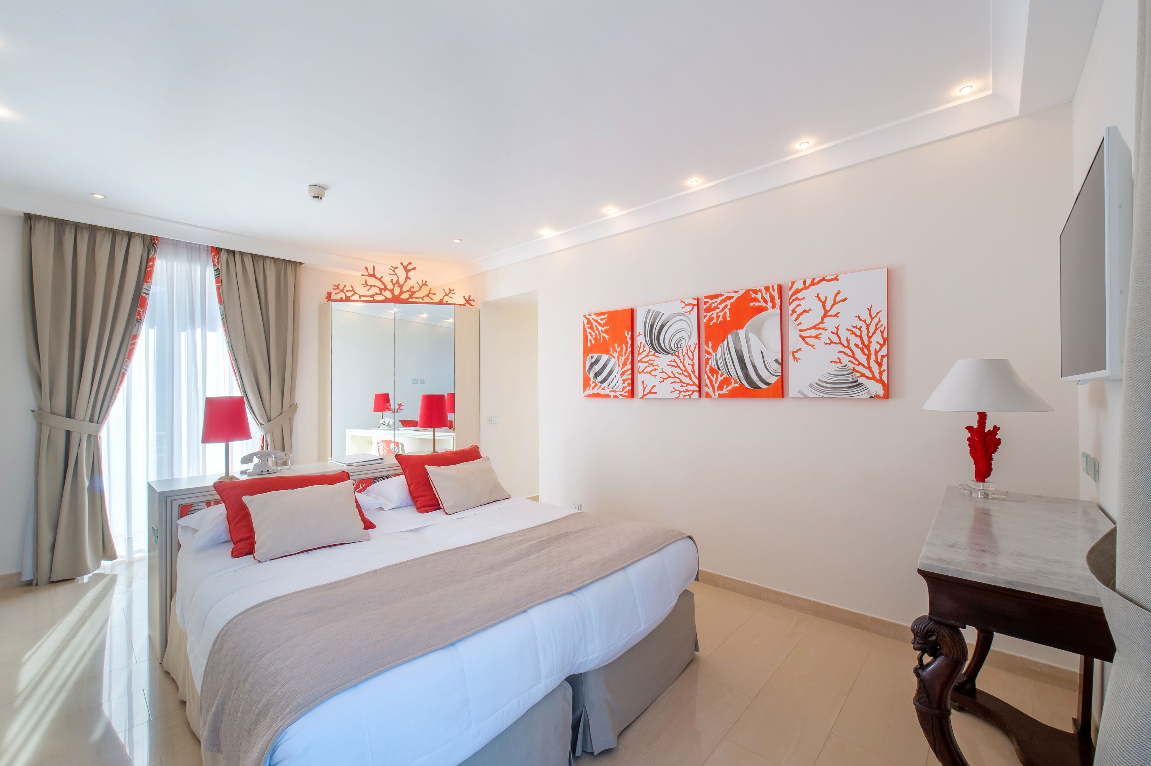 A modern hotel room with a large bed, a bedside table, a mirror, and artwork on the wall.