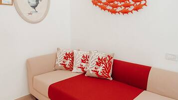 A room with a beige sofa, red and white patterned pillows, and a red heart-shaped decoration on the wall.