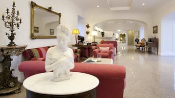 Amplio salón con una estatua de mármol como pieza central, un sofá rojo y un espejo grande.