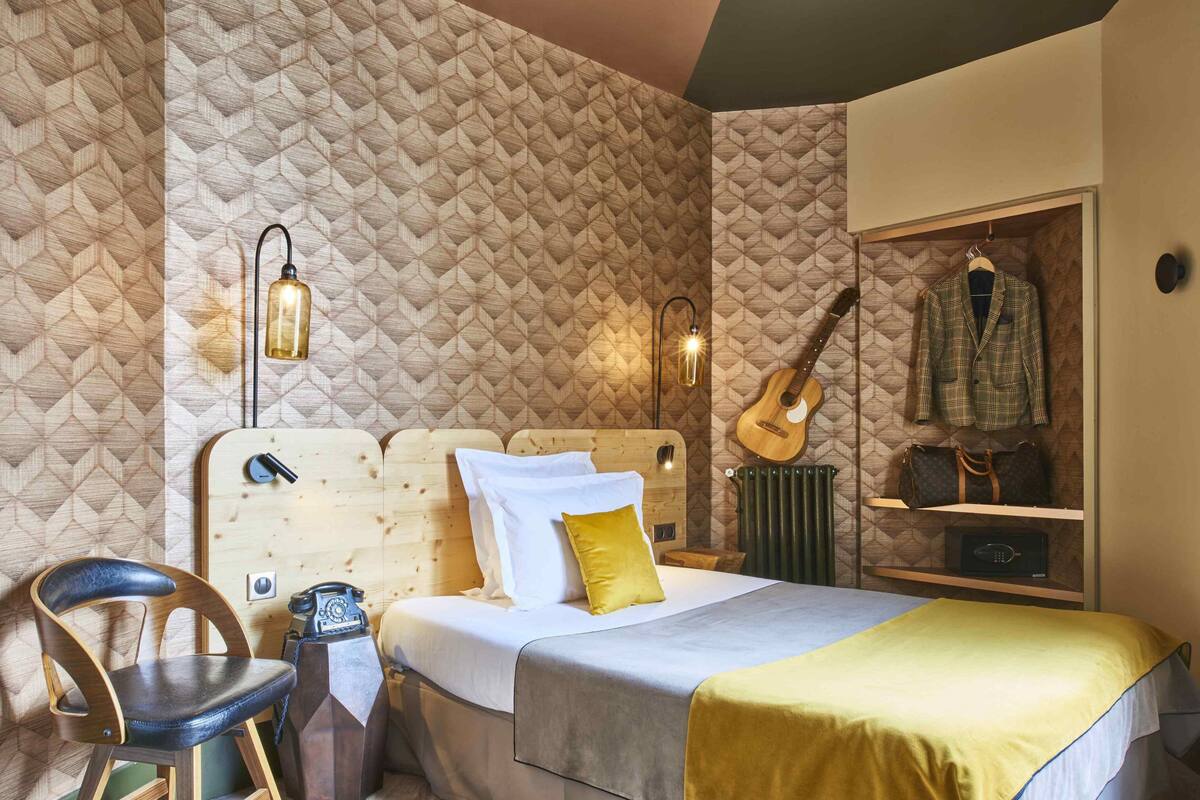 Ein Schlafzimmer mit einem Holzkopfteil, einem Bett mit weißer und gelber Bettwäsche, einer Gitarre und einem an der Wand befestigten Kleiderhaken.