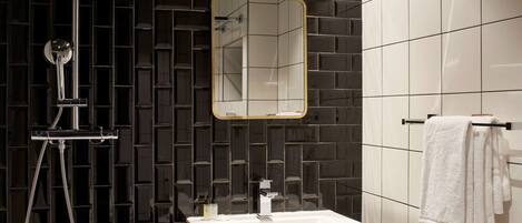 A modern bathroom with a dark tiled wall, a white sink, a mirror, and a towel rack.