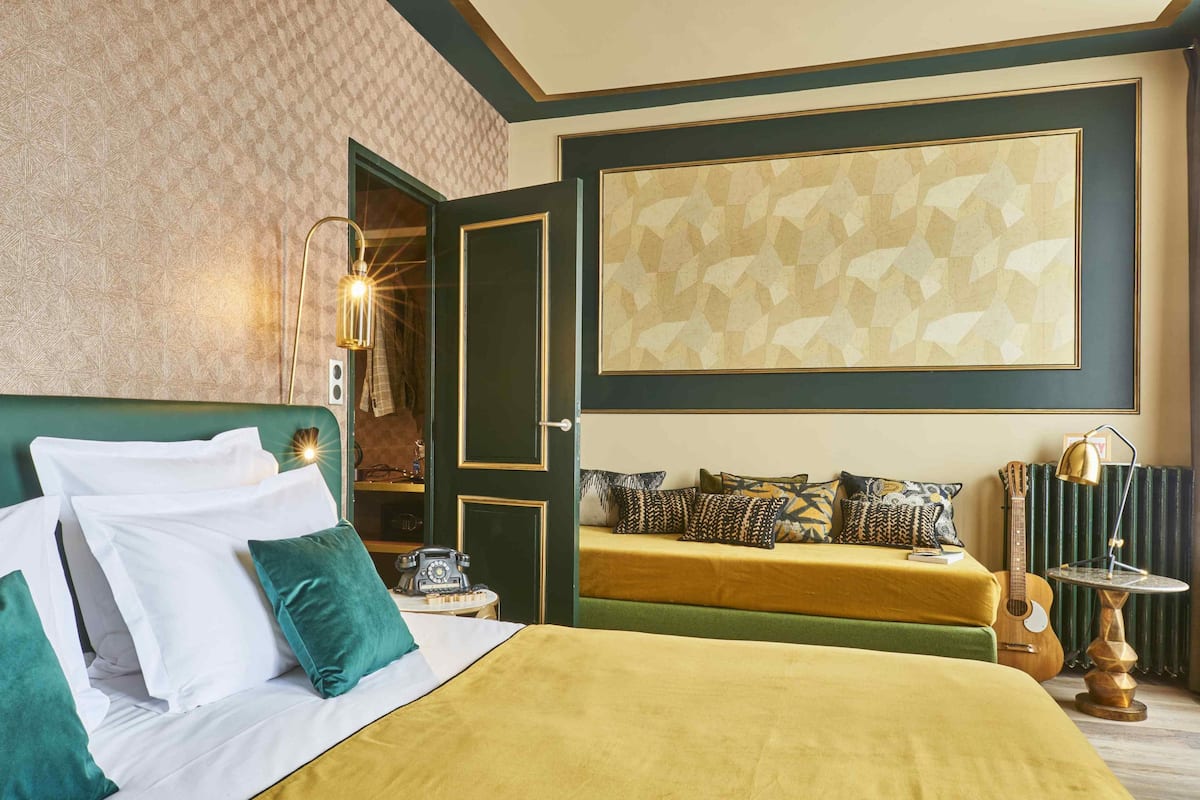 Ein Hotelzimmer mit Bett, Nachttisch, Lampe, einer Gitarre und einem großen abstrakten Gemälde an der Wand.