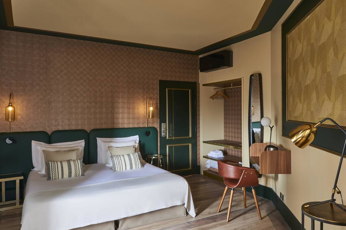 Ein Hotelzimmer mit einem Bett, einem Sessel, einem Schreibtisch, einem Spiegel und einer Lampe.