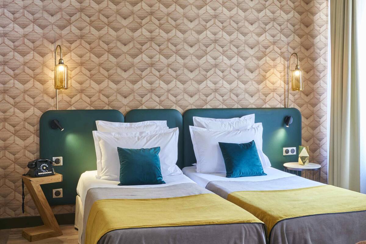 Ein Hotelzimmer mit zwei Betten, einem hölzernen Nachttisch, einem Telefon und einem kleinen Tisch mit einer Lampe.