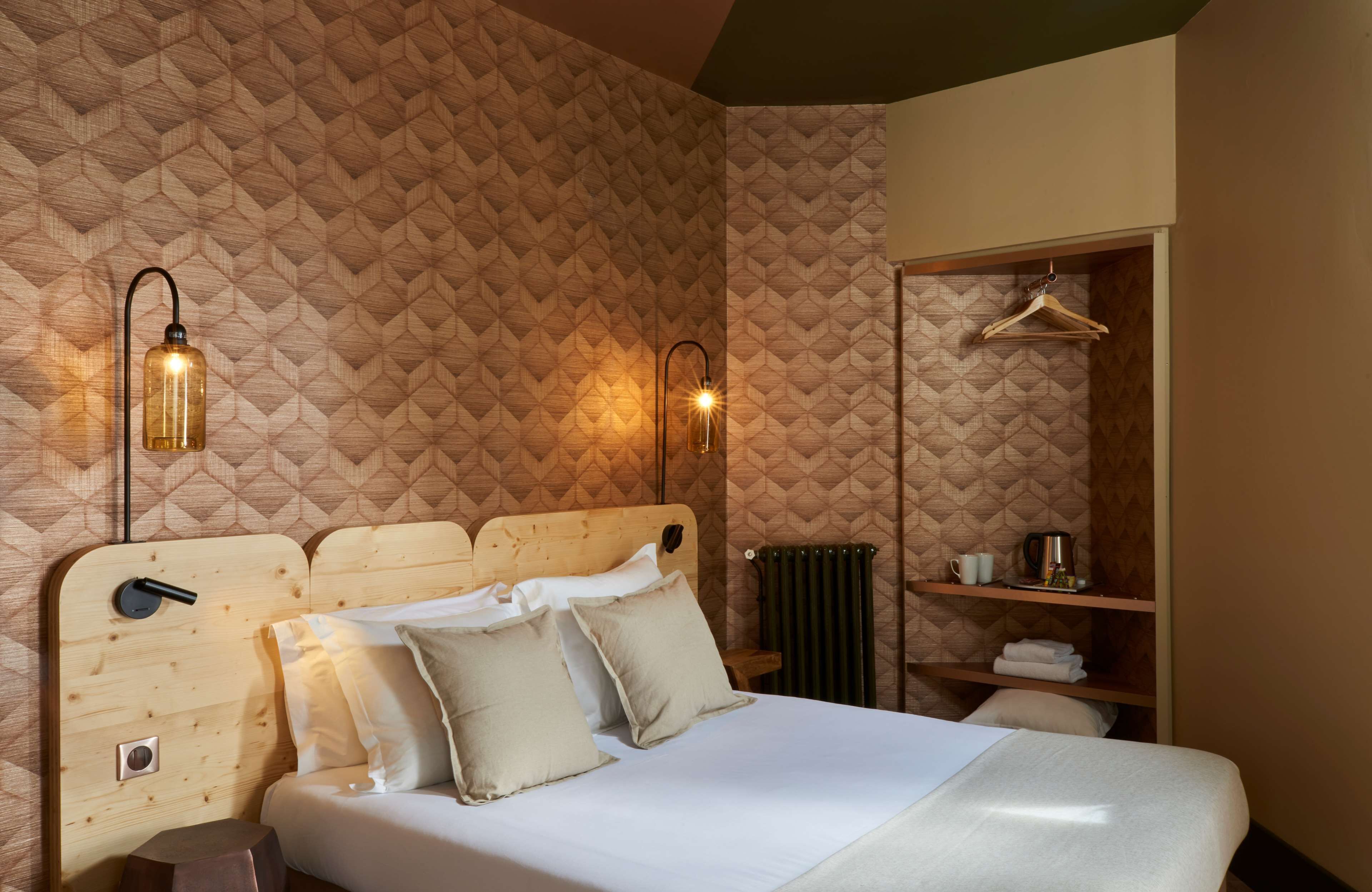 A neatly made bed with pillows, a wooden headboard, and two wall-mounted light fixtures.