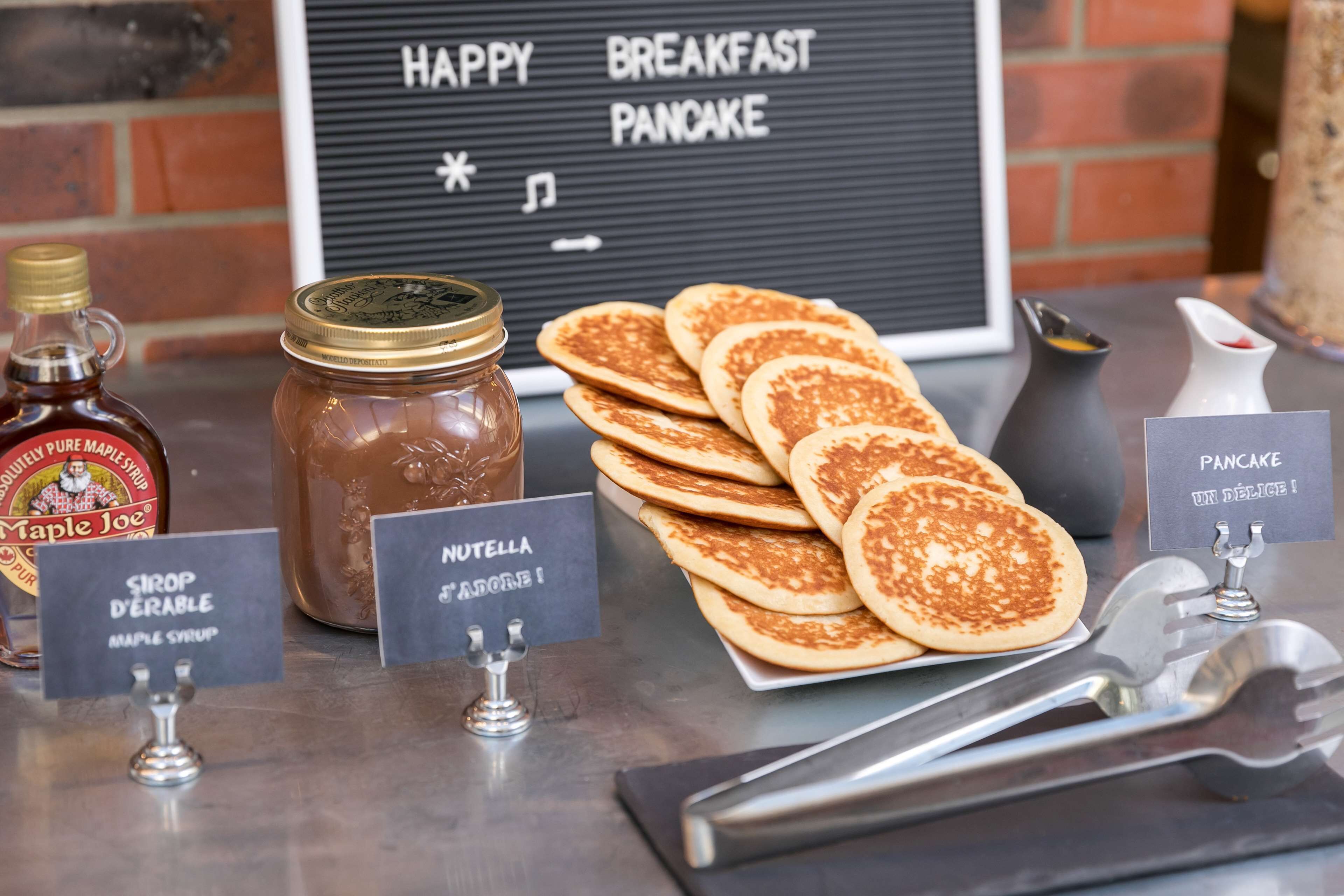 Ein Frühstückstisch mit Ahornsirup, Nutella und Pfannkuchen.