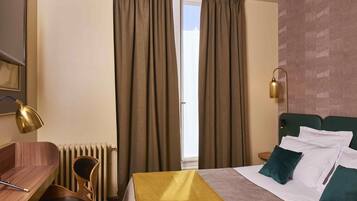 Una camera d'albergo con un letto, una scrivania, una sedia, una lampada e una finestra con tende.