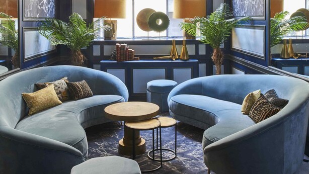 Eine luxuriöse Lounge mit einem großen Bogenfenster, blau gepolsterten Sitzgelegenheiten und einem runden Tisch in der Mitte.