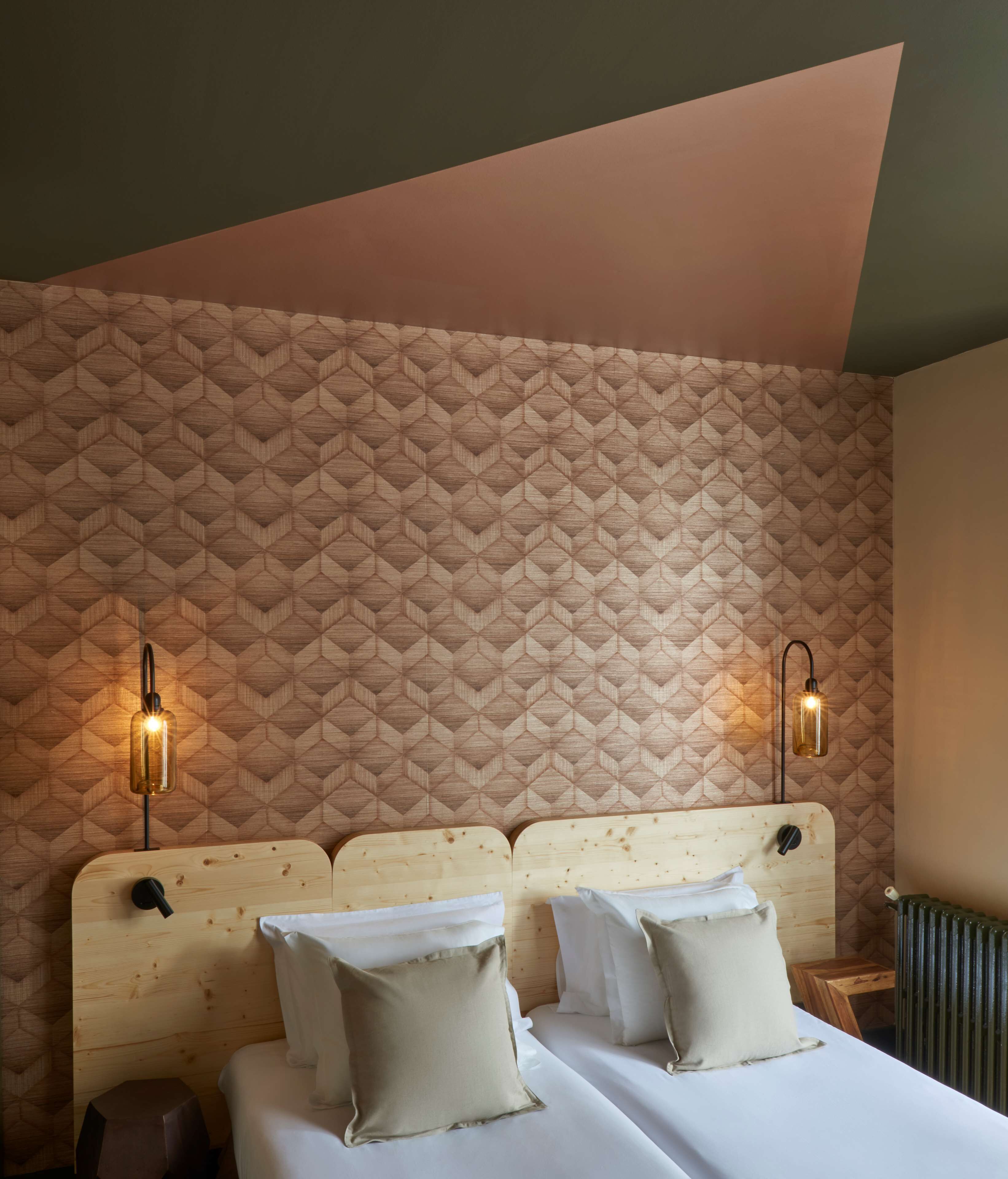 A hotel room with a geometric patterned wall, a wooden headboard, two bedside tables, and two wall-mounted lamps.