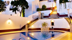 A large, white building with a swimming pool, a staircase, and a palm tree.