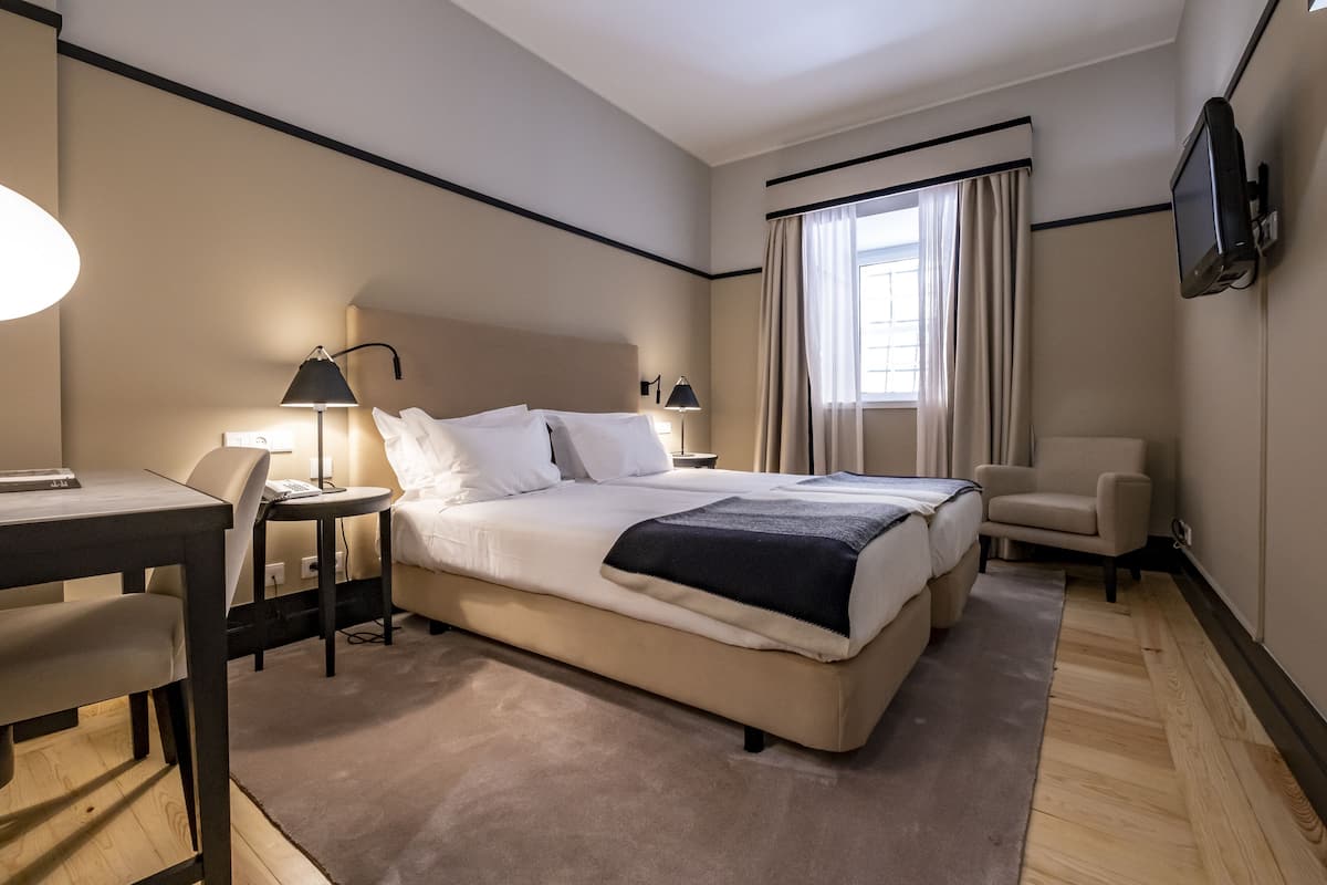 A hotel room with a large bed, a desk, a chair, a TV, and a window with curtains.