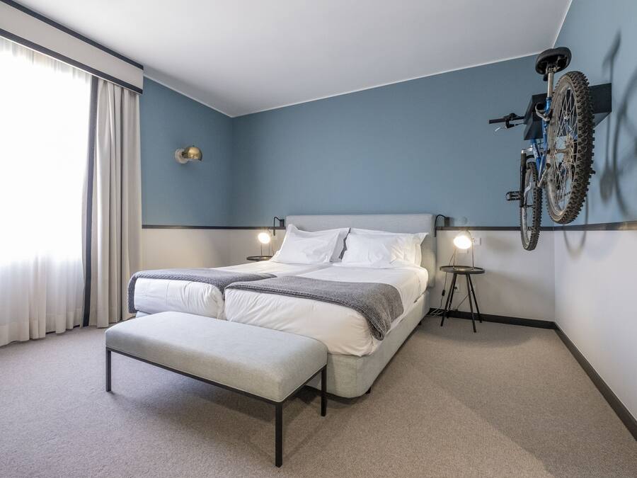 Et moderne hotelværelse med en stor seng, en bænk, en cykel monteret på væggen og et lille bord med en lampe.