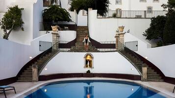 A pool area with a central staircase, lounge chairs, and a fountain.