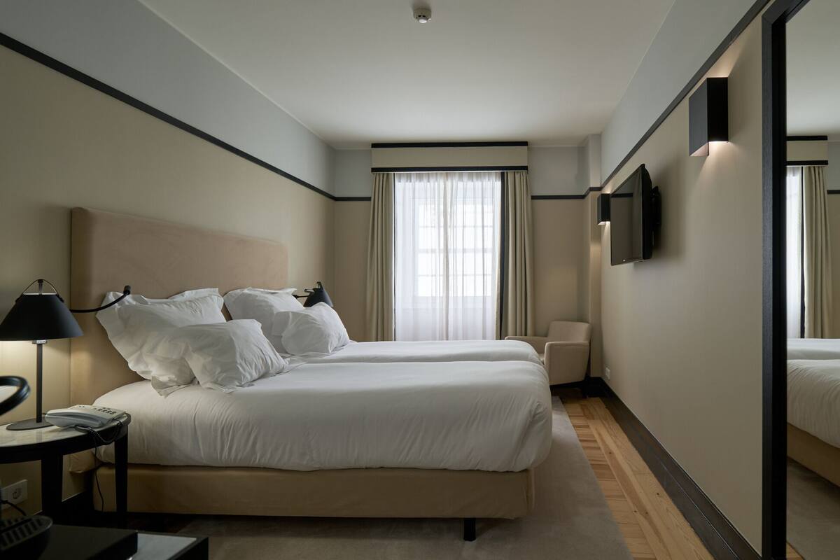 A hotel room with two beds, a desk with a lamp, a TV, and a large mirror.