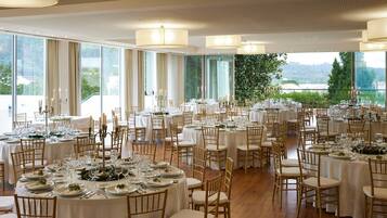 A large banquet hall with multiple round tables set for dining, featuring white tablecloths and candle centerpieces.
