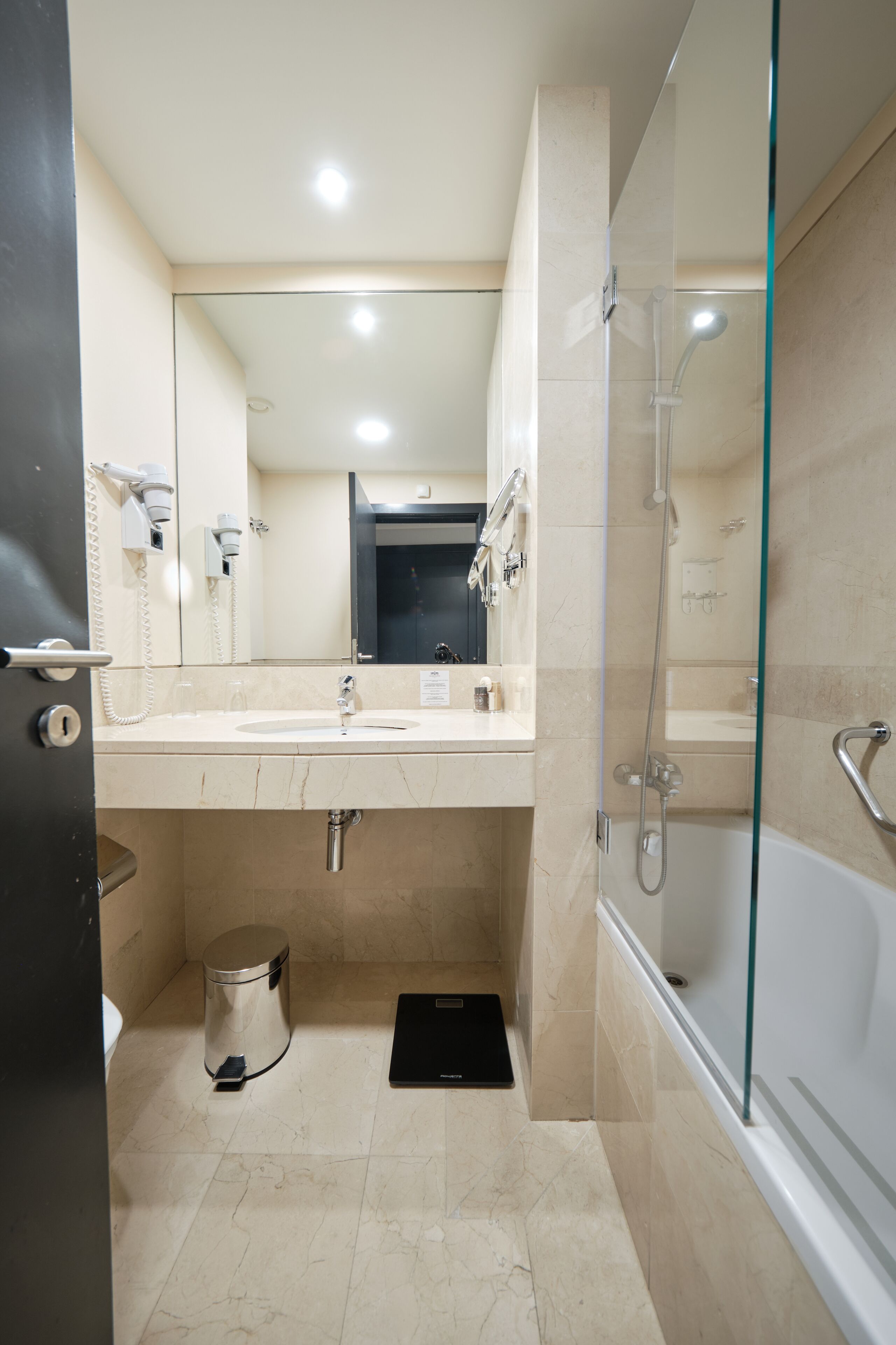 A modern bathroom with a glass shower enclosure, a sink, and a trash bin.