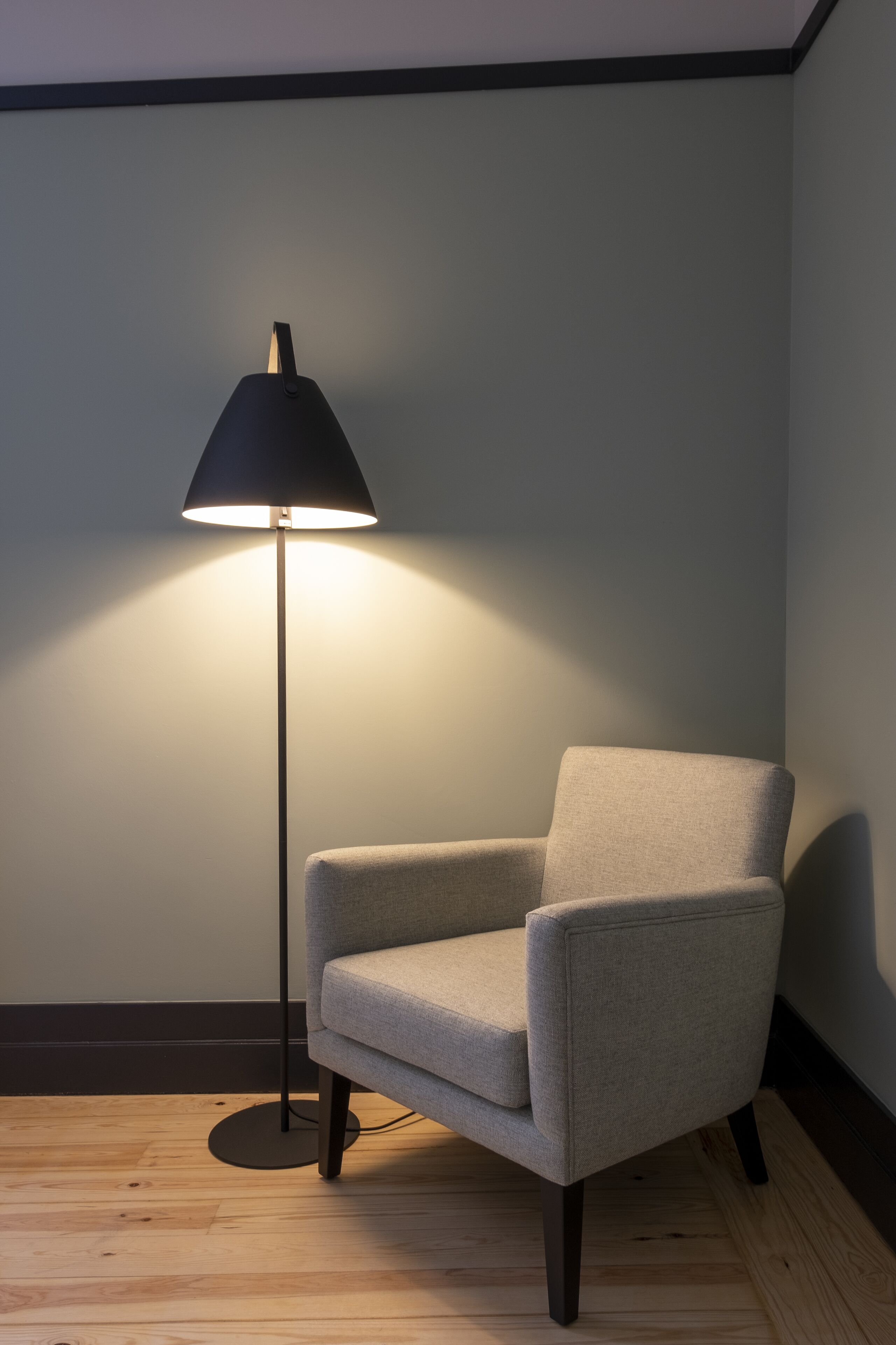 Ein Eckzimmer mit grauem Sessel, einer Stehlampe und Holzboden.