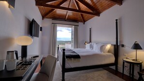A bedroom with a bed, bedside table, lamp, and a view of the outdoors.