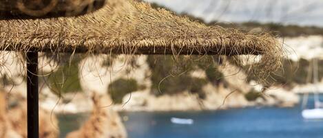 A thatched roof structure with a view of a coastal landscape and a boat in the distance.
