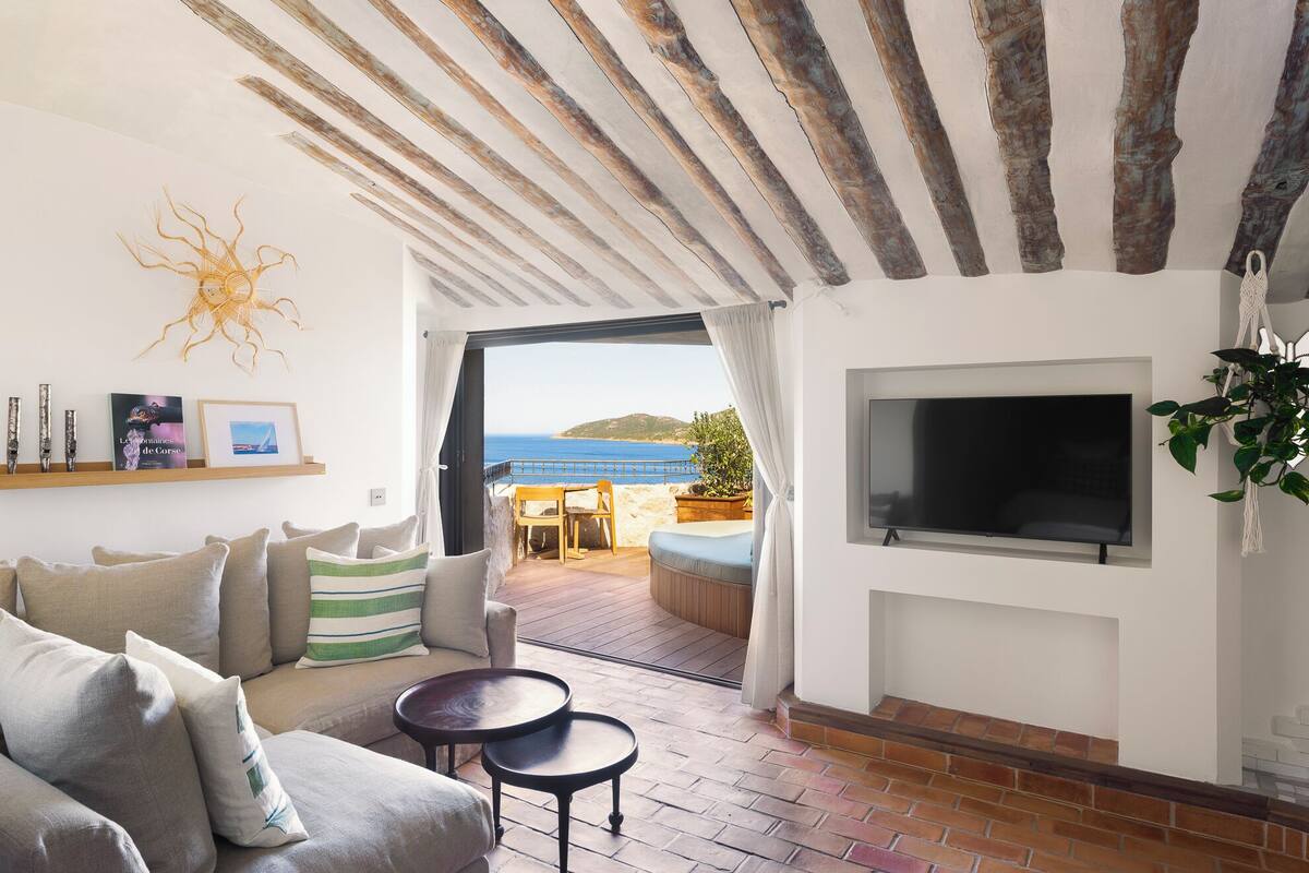 Sala de estar con sofá, televisión montada en la pared y vista al mar.