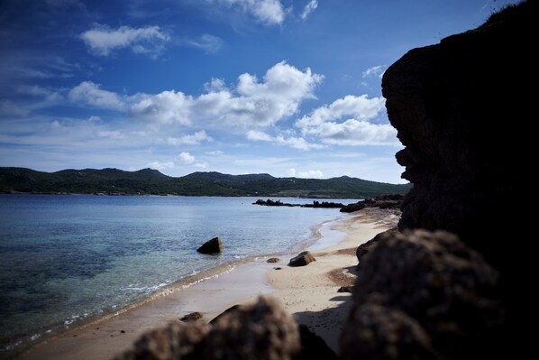 A beach with clear water, rocks, and distant hills. - U Capu Biancu (Bonifacio)