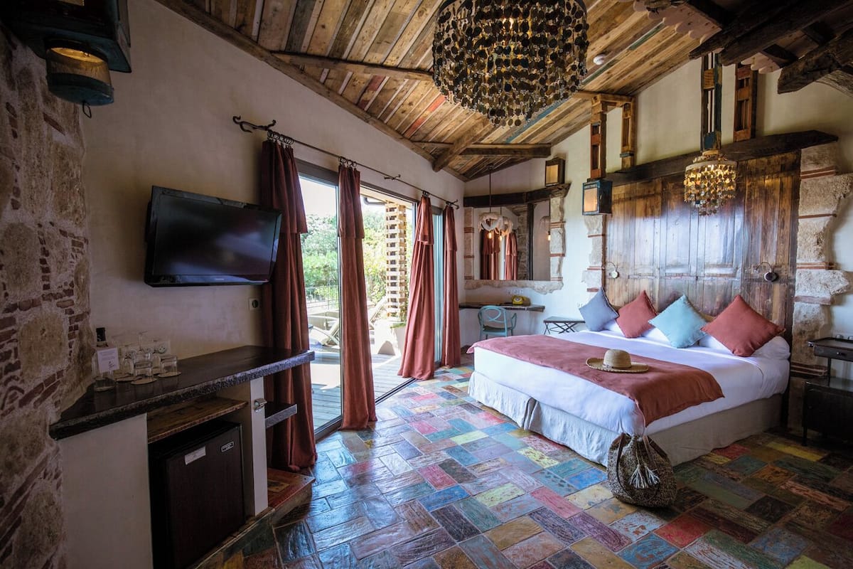 Un dormitorio rústico con techo de madera, una cama con almohadas coloridas, un televisor y vistas al exterior.