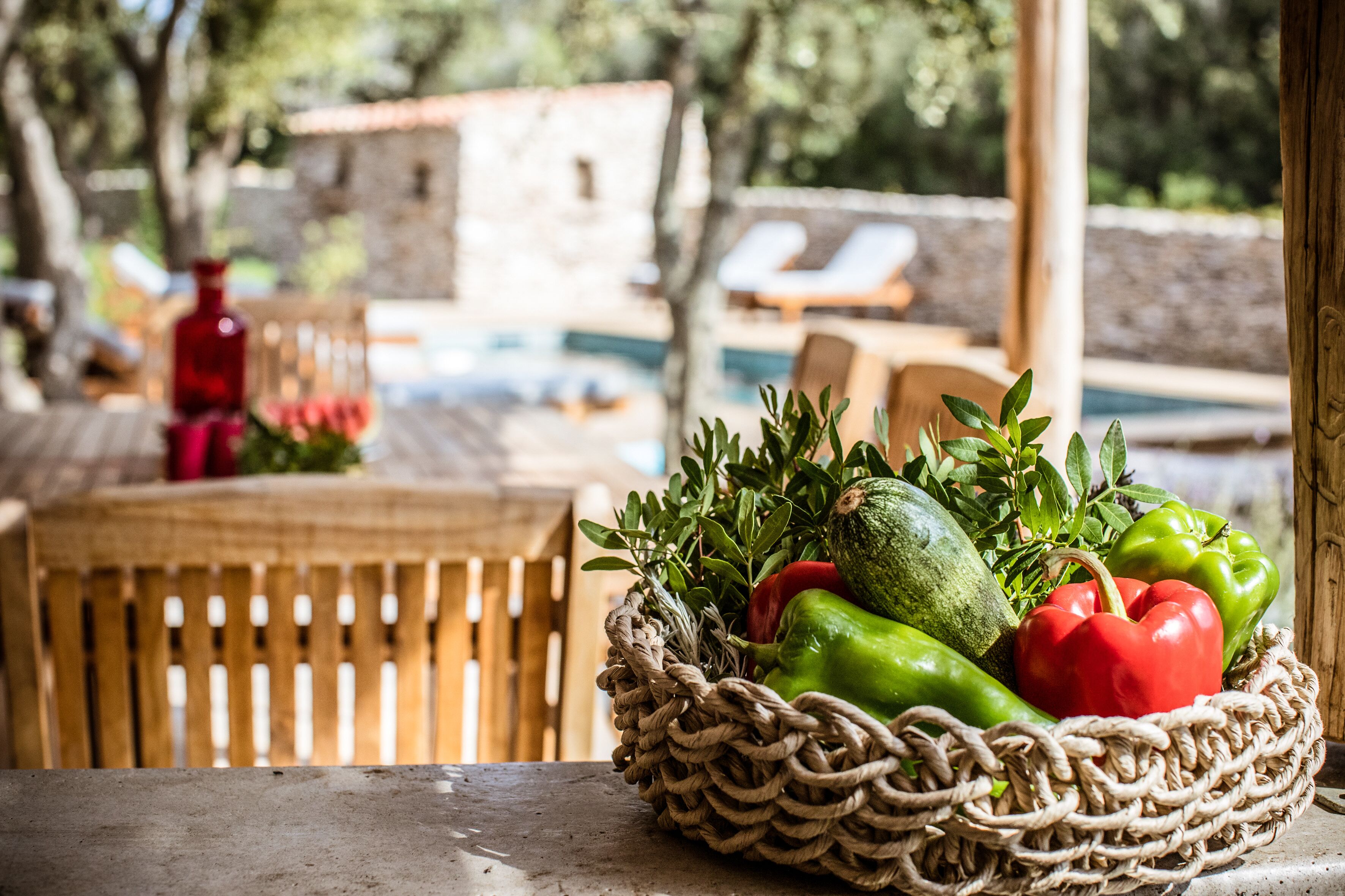 Ein Korbkorb mit Gemüse auf einem Tisch, im Hintergrund ein Pool und Liegestühle.