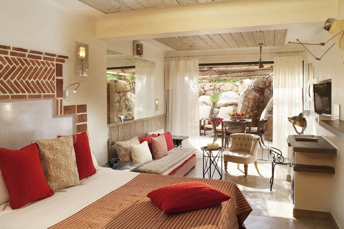 Un dormitorio con cama, sofá, mesa de comedor y sillas. Tiene pared de piedra y techo de madera.