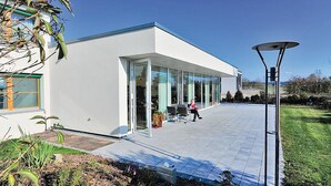 Un edificio moderno con amplios ventanales, techo plano y un patio empedrado.