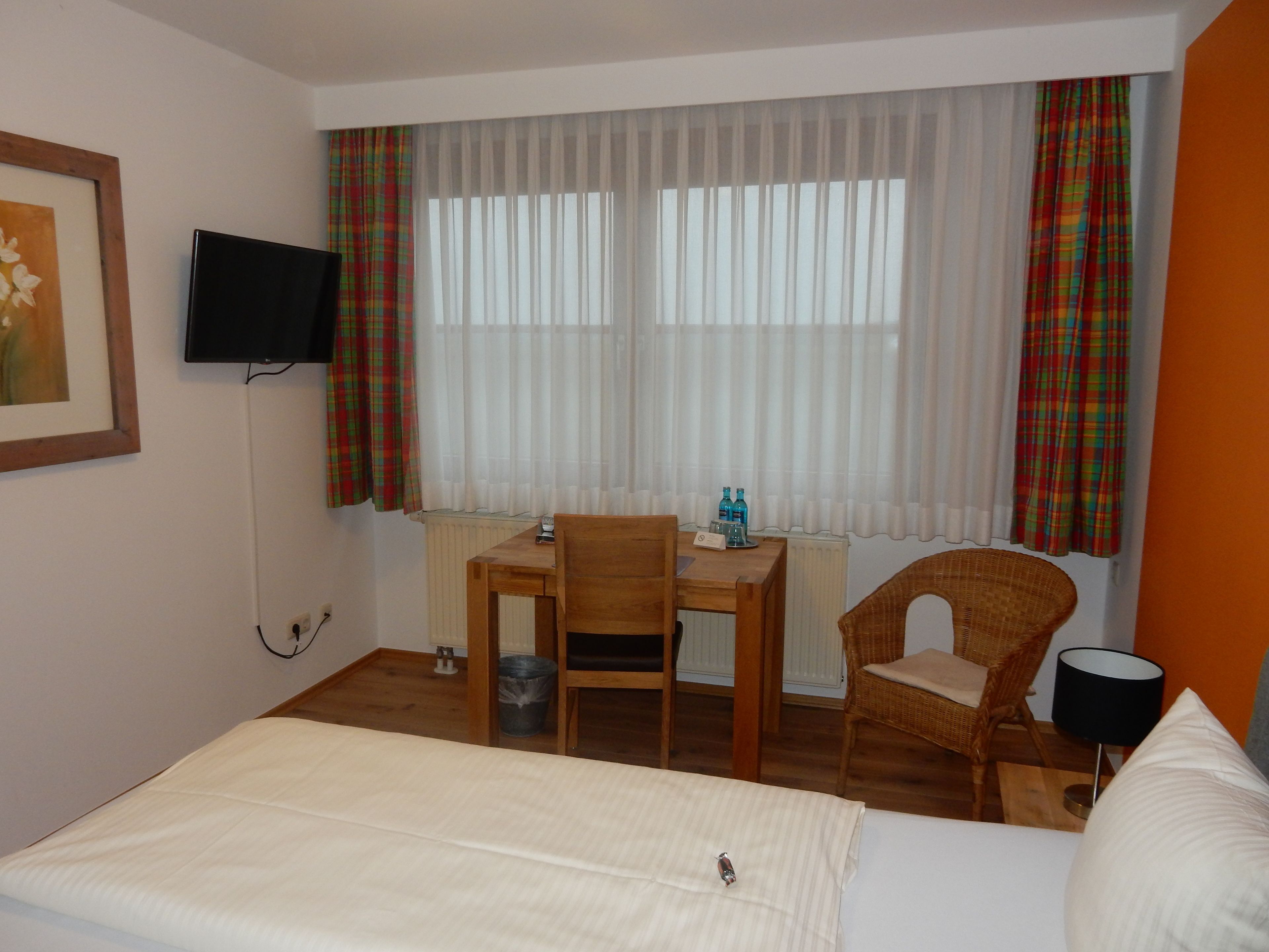 A hotel room with a bed, a desk with a chair, a television, and a window with curtains.