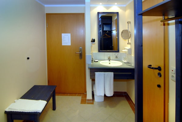 A bathroom with a wooden bench, a sink, a mirror, and a towel rack. - Hotel Frankenhöhe (Aurach)