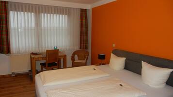 Habitación de hotel con cama, dos almohadas, escritorio con silla, lámpara y ventana con cortinas.