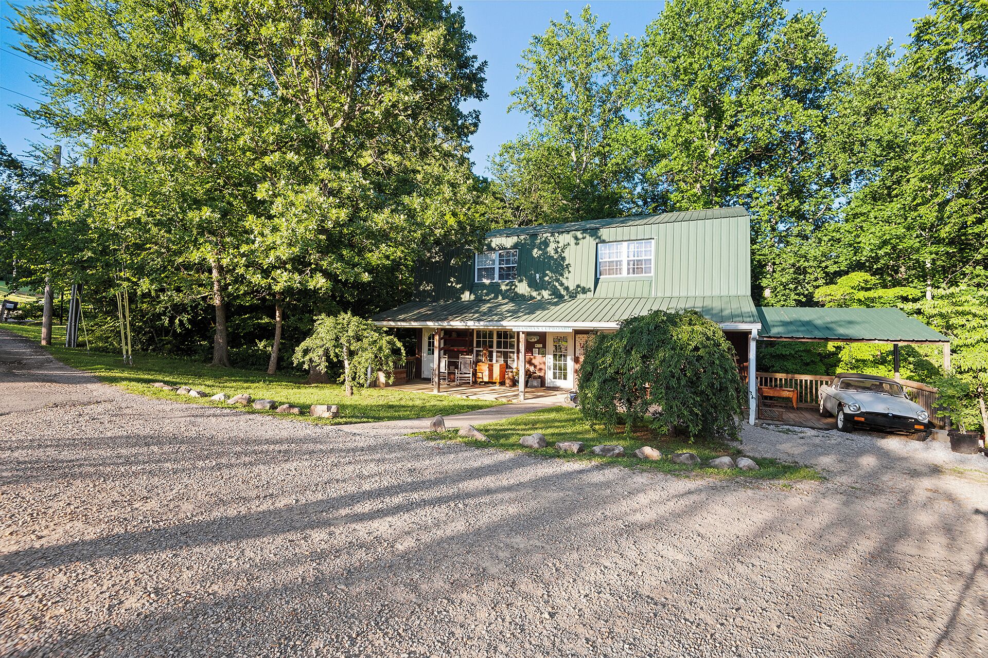 A two-story house with a porch, a car parked outside, and a gravel driveway.