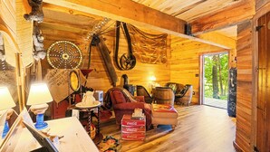 A cozy cabin interior with wooden walls, a wooden ceiling, a fireplace, a dining table, and a large window. - Nolichuckey Bluffs Cabins (Greeneville)