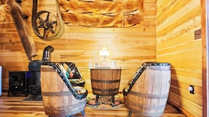 A wooden interior with two barrel-shaped stools, a wooden wall with a fur-like pattern, and a rustic stove. - Nolichuckey Bluffs Cabins (Greeneville)