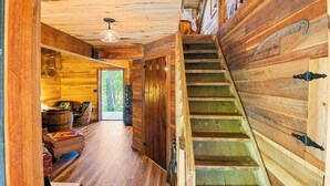 A wooden interior with a staircase, a door leading outside, and a ceiling light fixture. - Nolichuckey Bluffs Cabins (Greeneville)