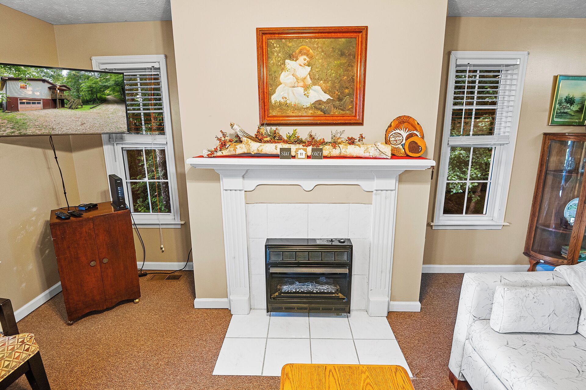 A living room with a fireplace, a painting above it, and a small shelf with decorative items.