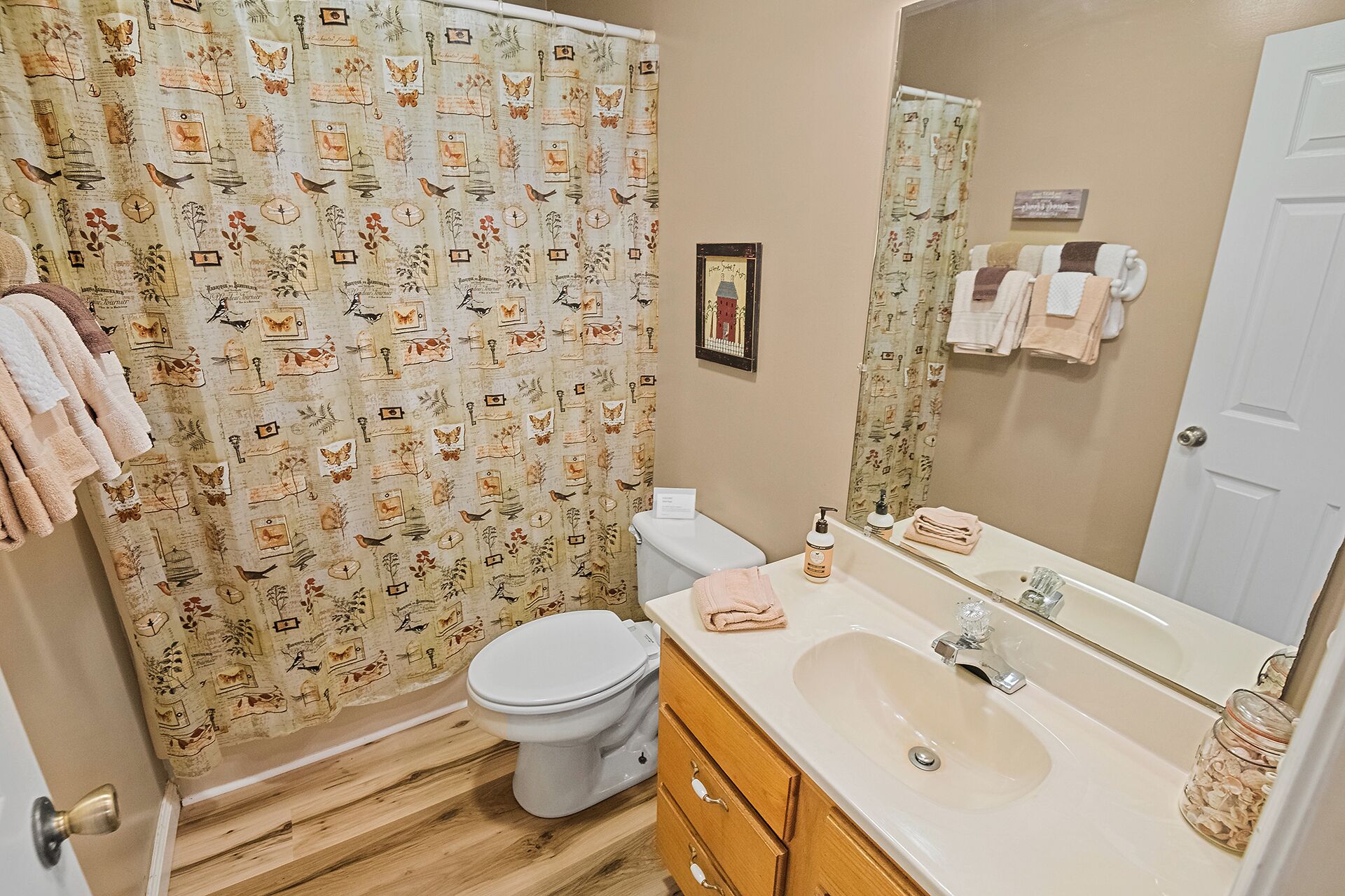 A bathroom with a patterned shower curtain, a toilet, a sink with a mirror, and wooden cabinets.