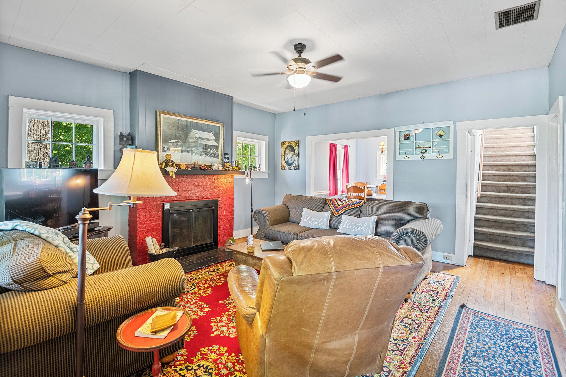 A living room with a fireplace, a sofa set, a television, and a ceiling fan.