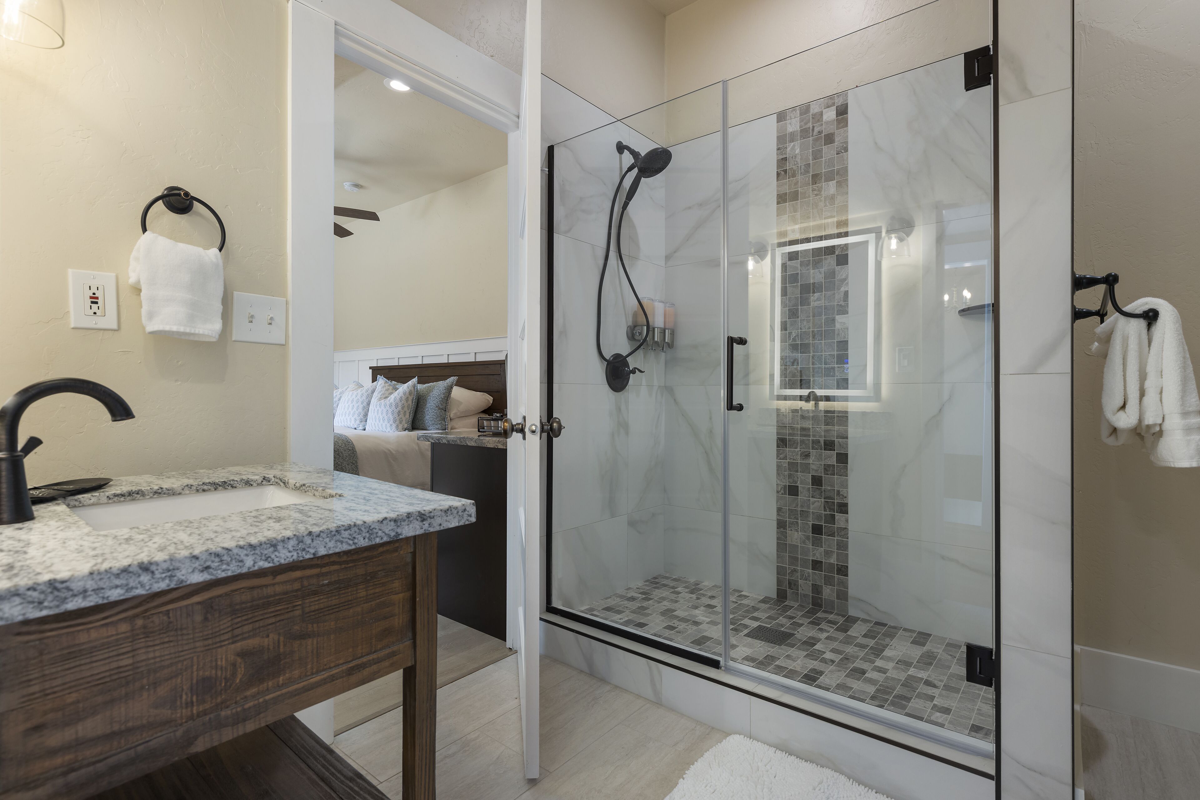Un baño moderno con ducha de vidrio, lavamanos de granito y tocador de madera.